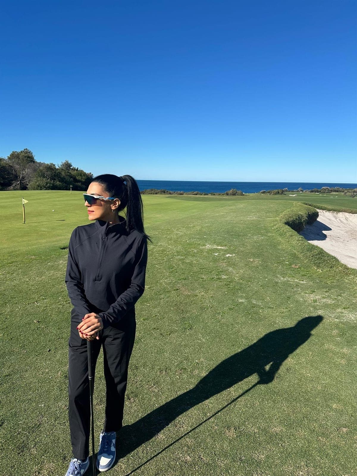 Rukmini Mehta leaning on a golf club on the coastal links at St Michael's Golf Club, overlooking the ocean